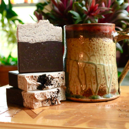Bars of brown and beige vegan Caffe Mocha soap seen alongside a mug of coffee, appropriate for a soap featuring scents of chocolate mocha and ground coffee.