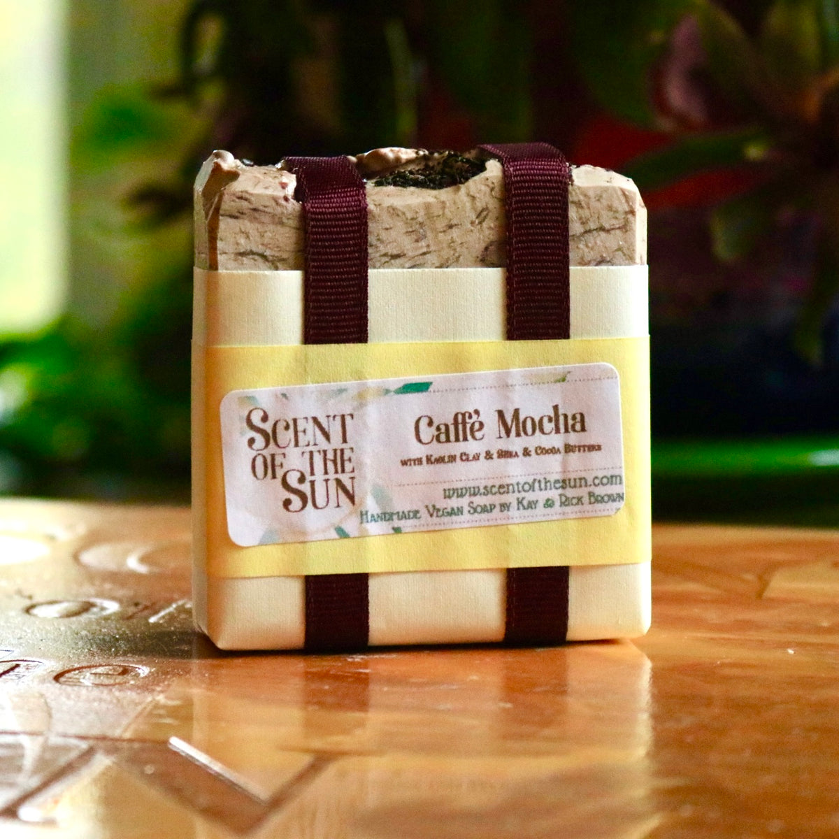 Wrapped bar of plant-based Caffe Mocha soap with dark maroon ribbon holding together a paper covering on a wooden background.