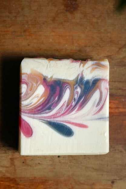 Bar of vegan, plant-based Winter Maiden bar soap atop a wooden background. This soap features aromas of pine, smoke, peppermint, and mistletoe. 