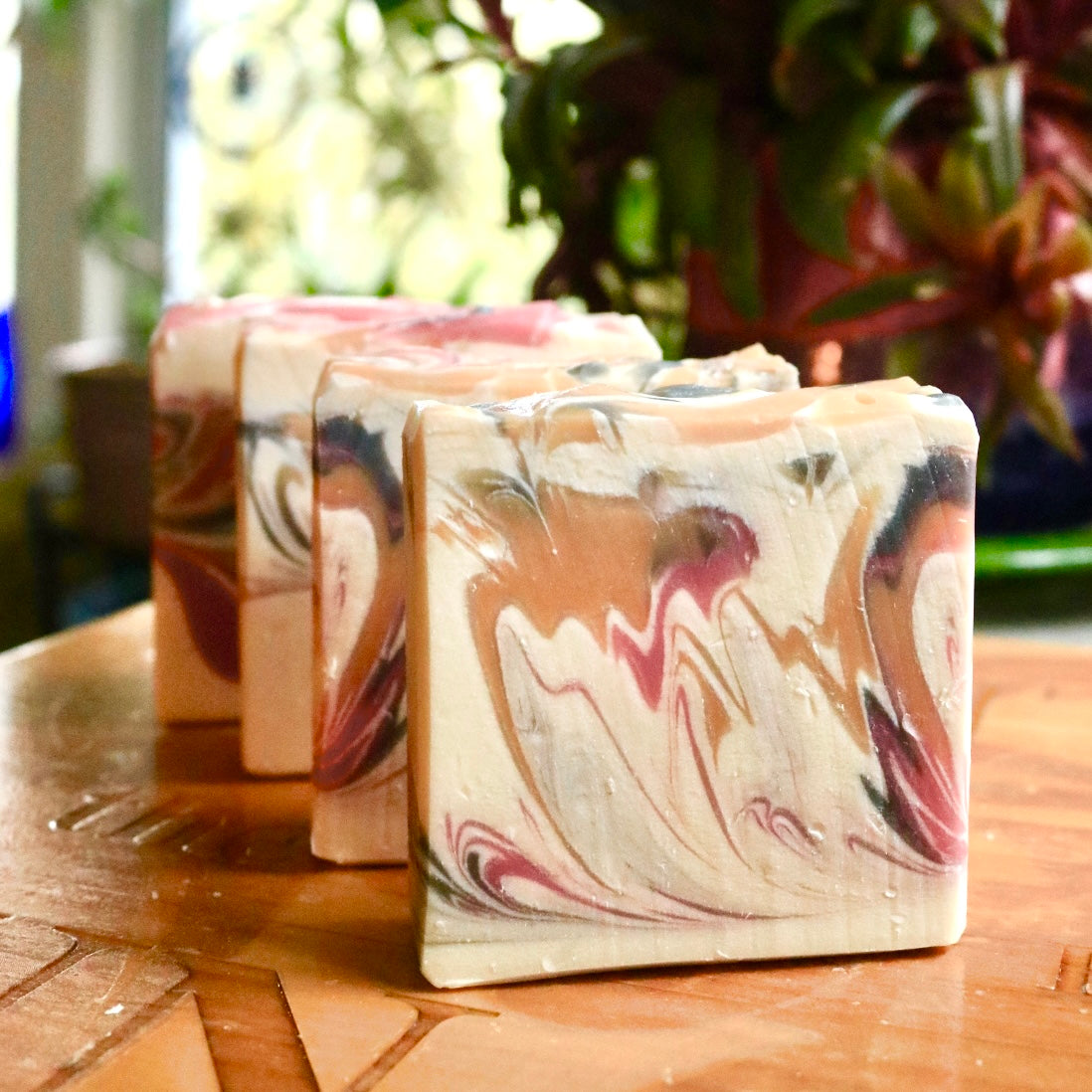 Four bars of vegan, plant-based Winter Maiden soap, a wintery, crisp scent, seen from the front on a wooden base with a background of green plants.