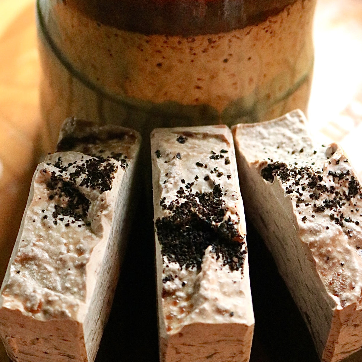 Three bars of vegan, plant-based Caffe Mocha soap seen in front of a coffee mug atop a wooden background.