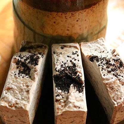 Three bars of vegan, plant-based Caffe Mocha soap seen in front of a coffee mug atop a wooden background.