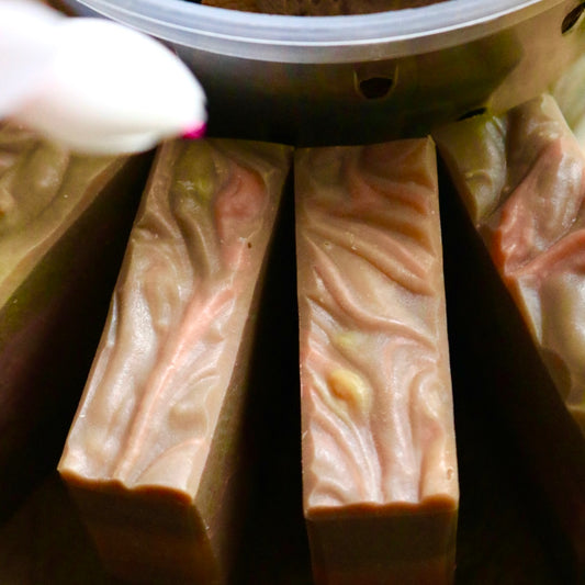 Sweet Fig vegan bar soaps seen from above, in front of what appears to be a plant container. The top is mottled with swirls of pink, brown, and yellow.
