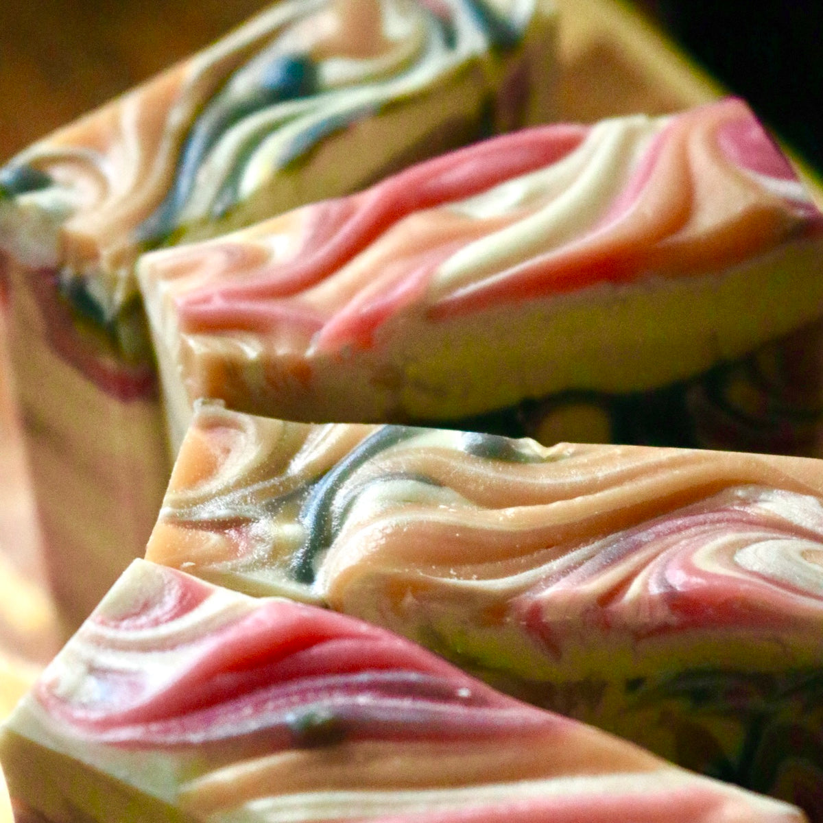 Four bars of plant-based vegan Winter Maiden soap seen from above with vibrant red, white, yellow, and black swirls in front of a wooden background.