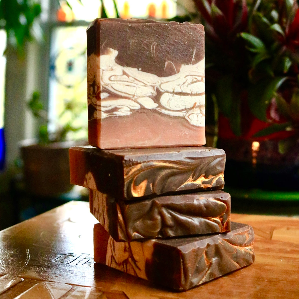 Stack of four vegan Chai Tea bar soaps, with the top plant-based bar standing atop three soaps on their side in front of a background of plants. Each bar features cruelty-free ingredients.