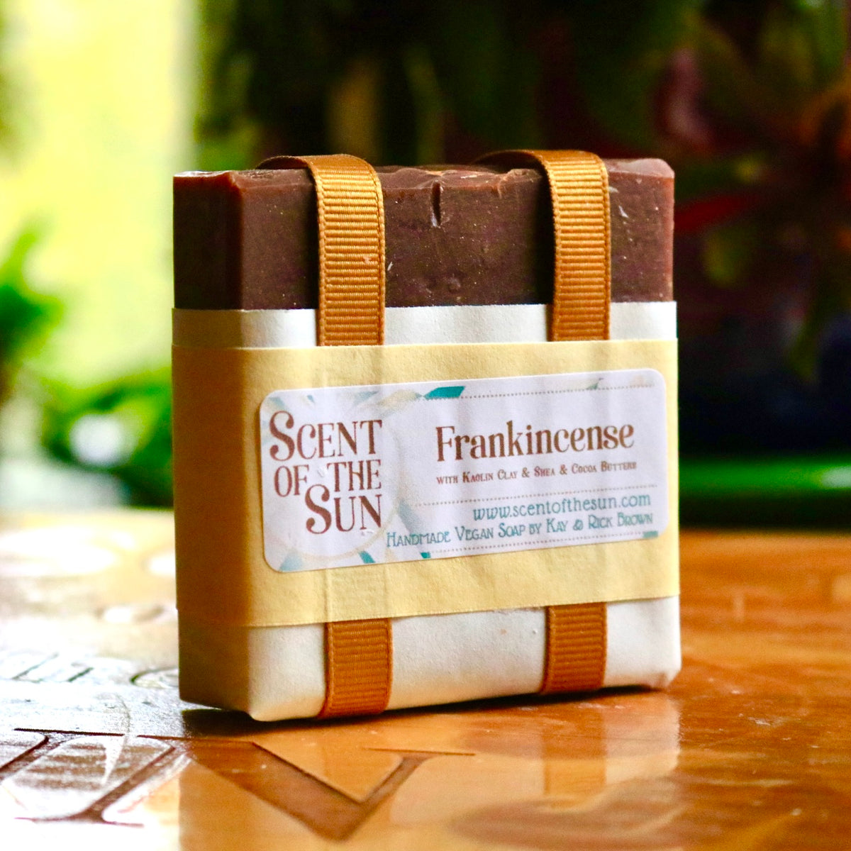 Wrapped bar of vegan Frankincense soap with a golden-orange ribbon and paper covering. The label states that the soap features kaolin clay, shea butter, and cocoa butter.